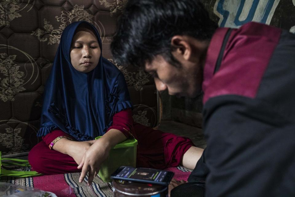 A woman in a blue hijab and red robe sits next to a man