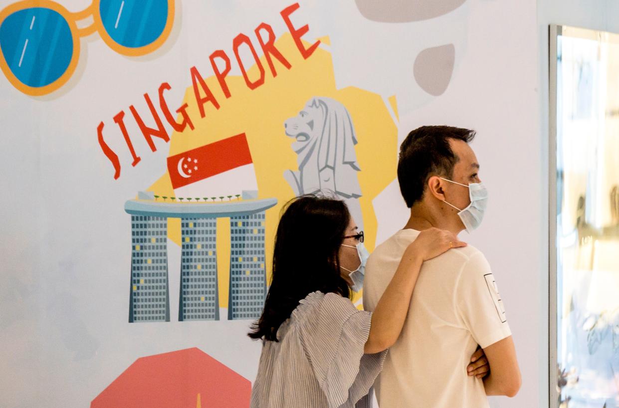 A couple, wearing protective facemasks amid fears over the spread of the COVID-19 coronavirus, walks in front of an advertisement board in Bangkok on 17 February, 2020, featuring attractions in Singapore. (PHOTO: AFP via Getty Images)