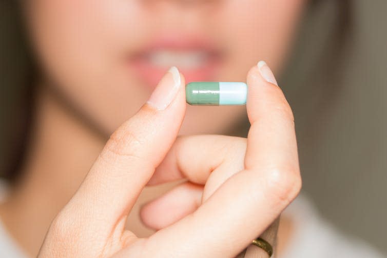 Woman holds an antibiotic pill between her thumb and index finger.