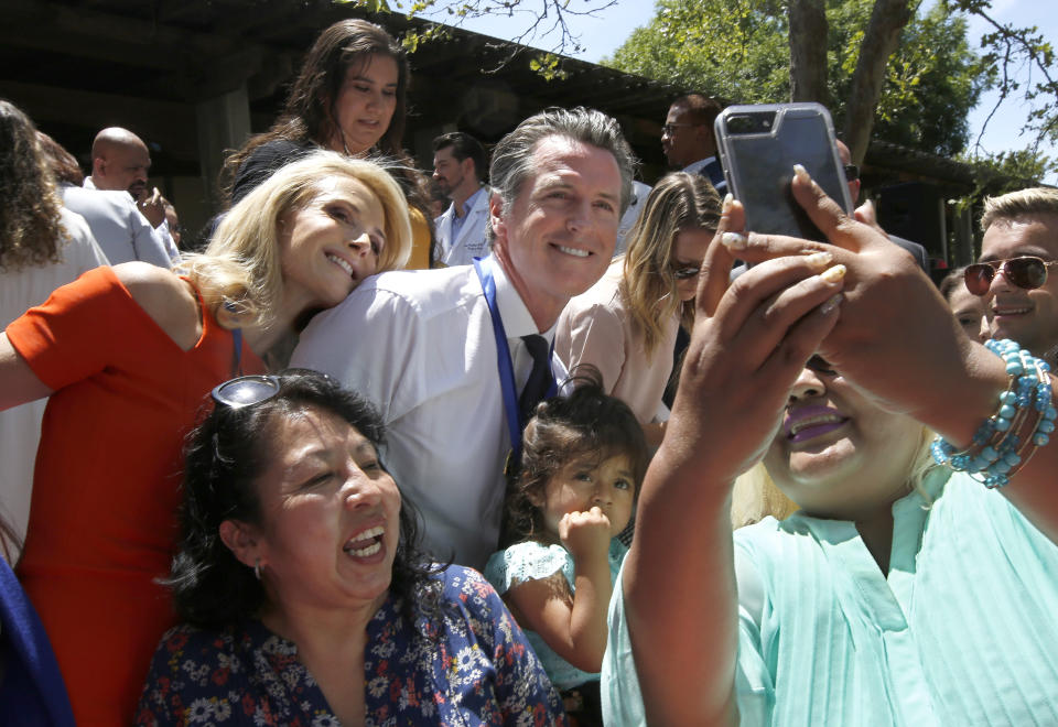 FILE-- In this July 1, 2019 file photo Gov. Gavin Newsom, center, poses for a photo with his wife, First Partner Jennifer Siebel Newsom, left, after signing several of the state budget trailer bills at Sacramento City College in Sacramento, Calif. Siebel Newsom has shunned the traditional title of "first lady" and is focusing on women's issues including equal pay and expanding family leave. (AP Photo/Rich Pedroncelli, File)