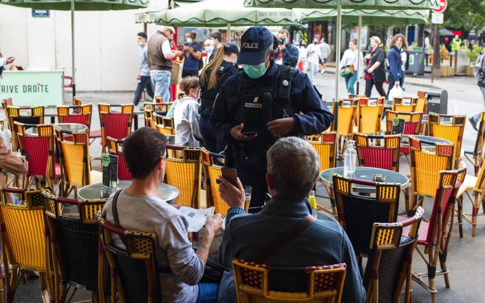 A French police officer conducts customer health pass document checks, enforced under new nationwide legislation, at a restaurant in Paris  - Bloomberg/Nathan Laine 