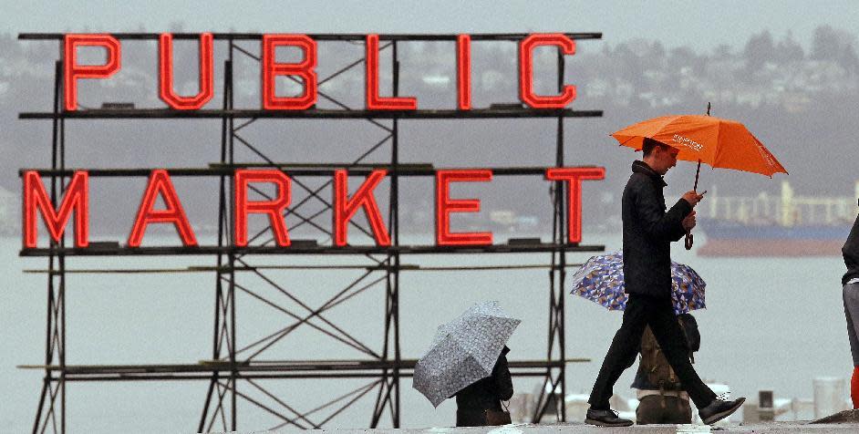 Pedestrians huddle under umbrellas as they walk past the Pike Place Market and in view of Elliot Bay behind, Wednesday, Jan. 18, 2017, in Seattle. Freezing rain, ice and fallen trees forced the closure of highways and roads in Oregon and Washington on Wednesday. Interstate 90, the main highway connecting western and eastern Washington, was to remain closed over Snoqualmie Pass until at least Thursday morning because of hazardous winter conditions. (AP Photo/Elaine Thompson)