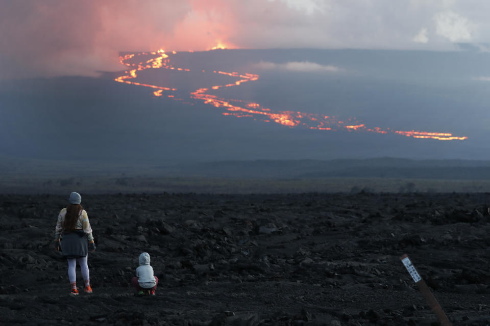 FILE - Spectators watch the lava flow down the mountain from the Mauna Loa eruption, Nov. 29, 2022, near Hilo, Hawaii. On Wednesday, Dec. 7, the lava from Mauna Loa, was 1.8 miles from Saddle Road, also known as Route 200 or Daniel K. Inouye Highway, scientists with the U.S. Geological Survey said. (AP Photo/Marco Garcia, File)