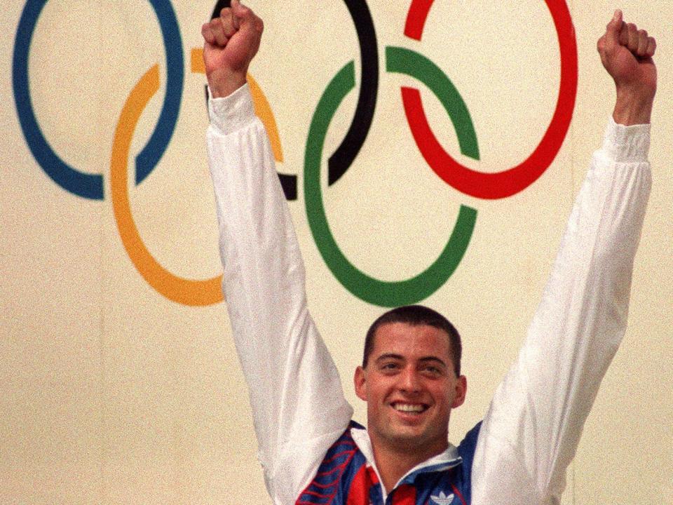 Matthew Biondi with his arms outstretched in the 80s with the olympic logo behind him