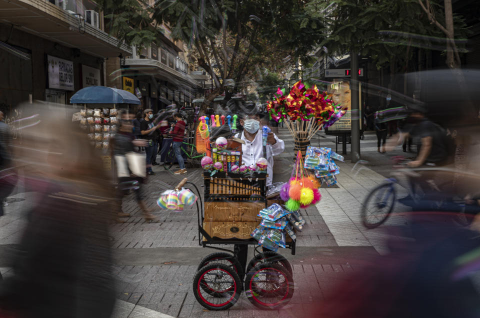 Un organillero lanza burbujas mientras toca música para pedir propinas y vende juguetes en el centro de Santiago, Chile, el viernes 28 de mayo de 2021, en medio de la pandemia de COVID-19. (AP Foto/Esteban Felix)