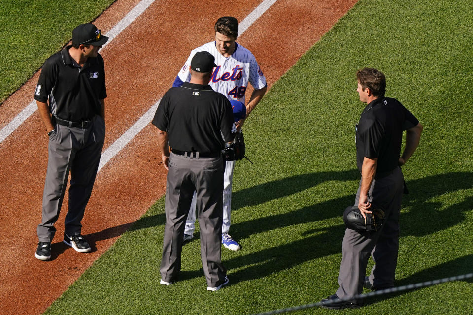 Third base umpire Ron Kulpa, bottom center, asks New York Mets starter Jacob deGrom, top center, about foreign substances before deGrom headed to the dugout after pitching in the first inning of a baseball game against the Atlanta Braves, Monday, June 21, 2021, in New York. Home plate umpire Ben May, right, looks on. (AP Photo/Kathy Willens)