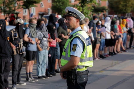 A police officer watches as masked protesters surround Bellahoj police station while they participate in a demonstration against the Danish face veil ban in Copenhagen, Denmark, August 1, 2018. REUTERS/Andrew Kelly