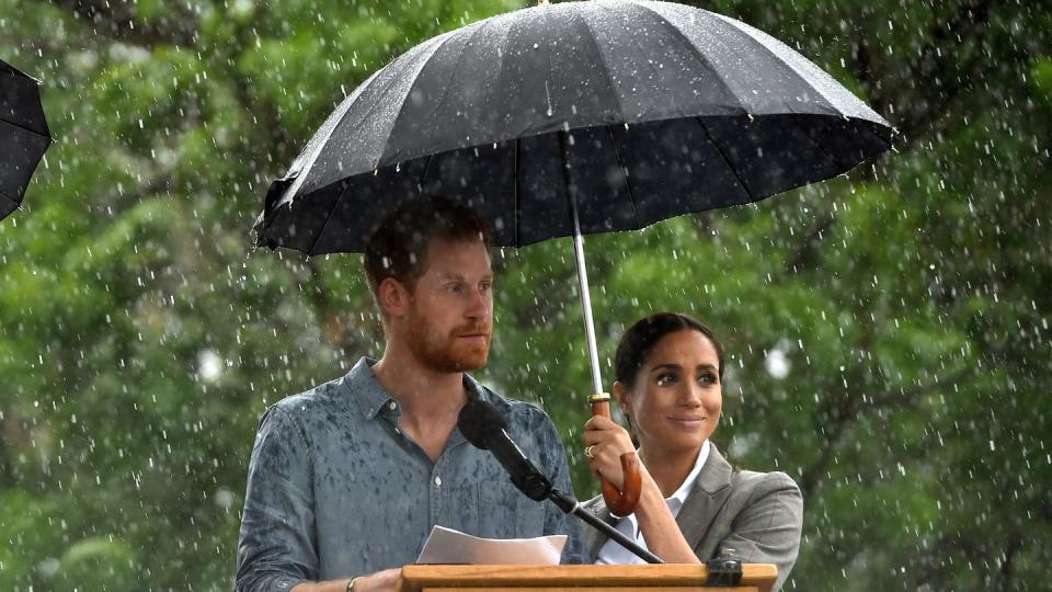 Prinz Harry neben Herzogin Meghan, die während eines Regenschauers einen Schirm hält, in Gubbo. Foto: Peter Parks