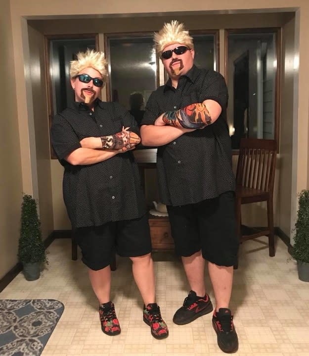 A woman and a man in black button downs and shorts with short blonde wigs, sunglasses, and tattoo sleeves