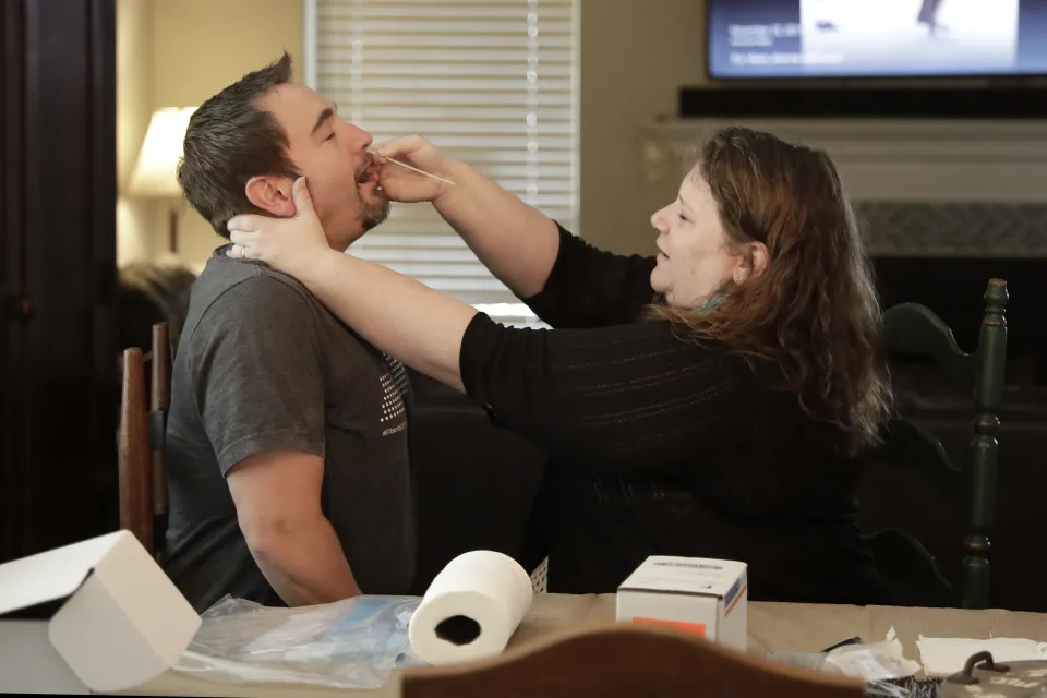 Mendy McNulty swabs the nose of her husband, Joe, in their home in Mount Juliet, Tenn., Tuesday, July 28, 2020. The family is participating in testing done twice a month to help answer some of the most vexing questions about the coronavirus. (AP Photo/Mark Humphrey)