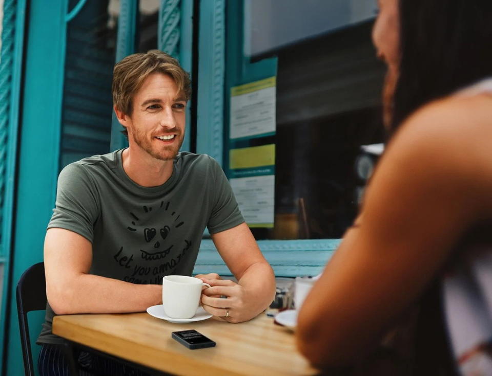 Two people use Timekettle's Fluentalk T1 at a café table to translate each other's language in real time.