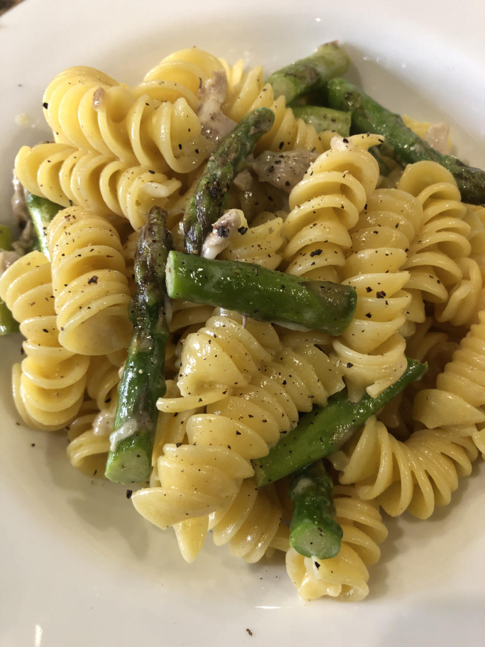 Close-up of a plate of rotini pasta mixed with asparagus spears and a creamy, peppered sauce