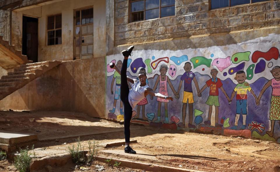 In this photo taken Friday, Dec. 9, 2016, Kenyan ballet dancer Joel Kioko, 16, strikes a pose as a joke as he walks through the courtyard of a school where he was teaching young dancers, in the Kibera slum of Nairobi, Kenya. In a country not usually associated with classical ballet, Kenya's most promising young ballet dancer Joel Kioko has come home for Christmas from his training in the United States, to dance a solo in The Nutcracker and teach holiday classes to aspiring dancers in Kibera, the Kenyan capital's largest slum. (AP Photo/Ben Curtis)