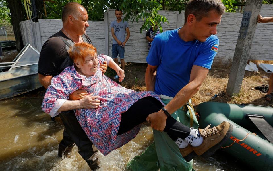 A member of Russia's emergencies ministry and a local resident carry an elderly woman during the evacuation of residents from a flooded area following the collapse of the Nova Kakhovka dam - ALEXANDER ERMOCHENKO/REUTERS