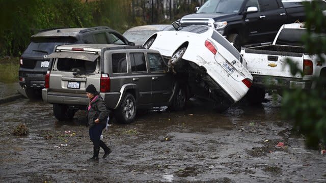 A woman walks by cars damaged by floods during a rainstorm in San Diego on Monday, Jan. 22, 2024.
