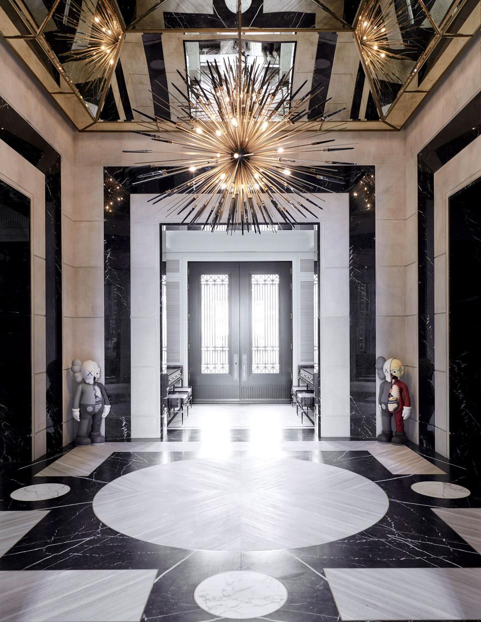 Two sculptures by Kaws flank the home’s entrance. Custom bronze-and-solid-marble chandelier by Rafauli; Escarpment Light and Nero Marquina marble cover the floor.