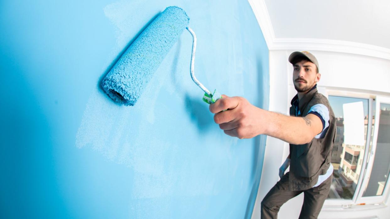 Young man painting a wall blue with a roller.