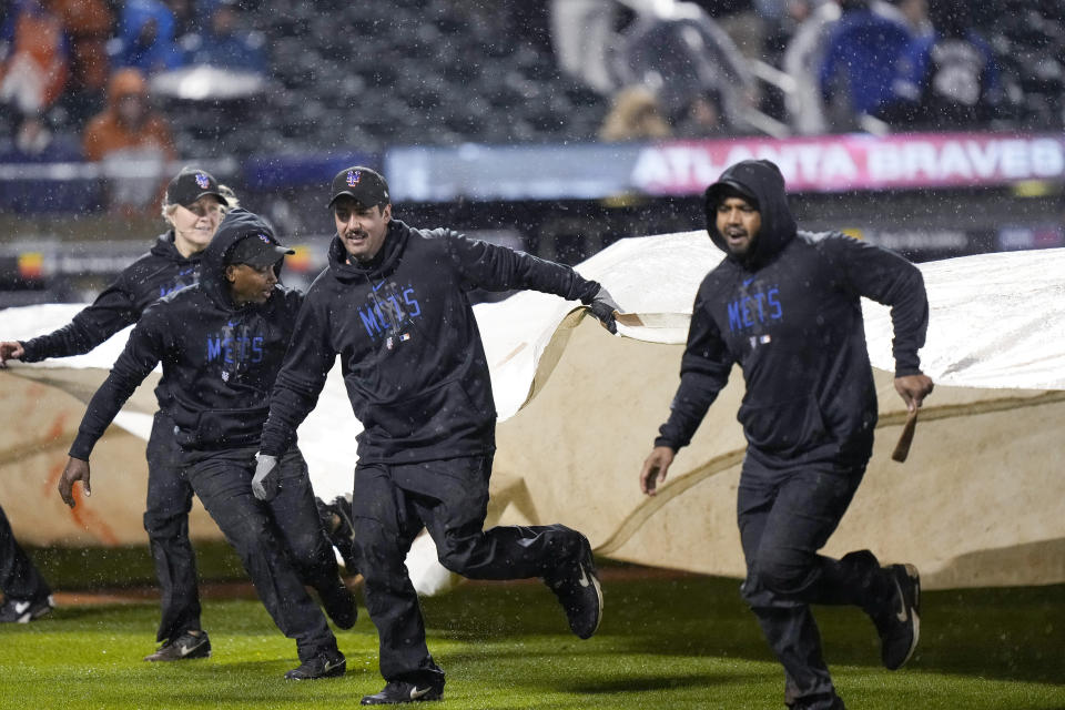 Members of the grounds crew cover the field with the tarp during a rain delay after the fifth inning of a baseball game between the New York Mets and the Atlanta Braves, Friday, April 28, 2023, in New York. (AP Photo/Bryan Woolston)