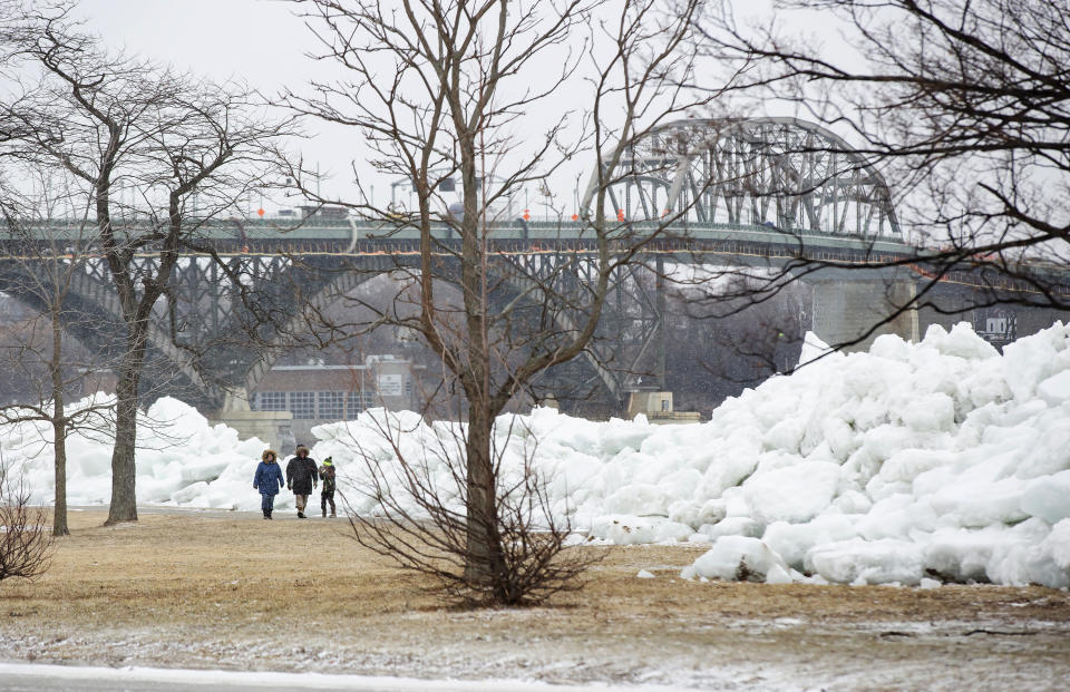 A family walks near a massive build up of ice that was pushed onto the shore of Mather Park in Fort Erie, Ont., Monday, February 25, 2019. A windstorm Sunday broke an ice boom in Lake Erie and allowed the ice, which was floating on the water at the mouth of the Niagara River, to shove over the retaining wall and onto the shore and the roadway above. (Tara Walton/The Canadian Press via AP)