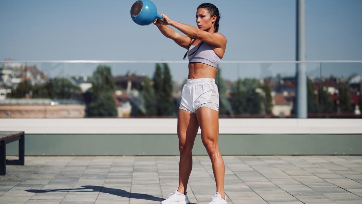  Woman outdoors performing a kettlebell swing with the weight in the air during kettlebell workout. 