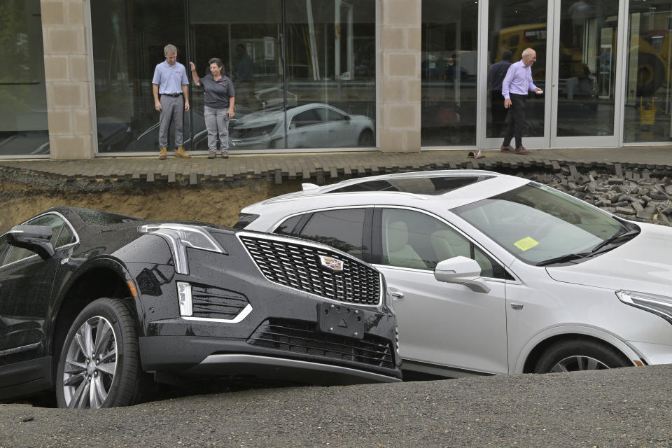 From left, car dealership owner Rick Durand Owner of Durand Cadillac and controller Michelle Bettez react beside three vehicles that fell into a sinkhole that was washed out of his car dealership Tuesday, Sept. 12, 2023, in Leominster, Mass. after more than 9 inches of rain fell overnight. (AP Photo/Josh Reynolds)