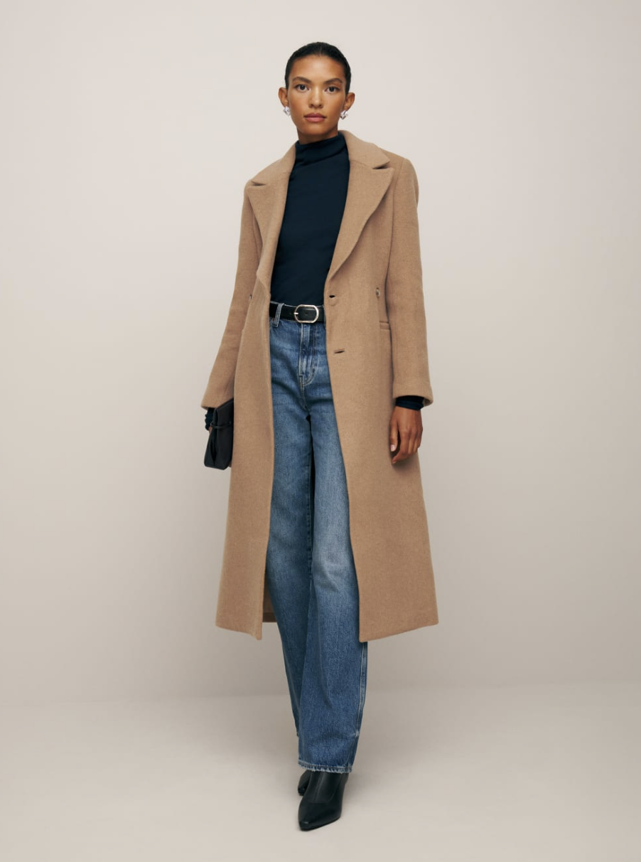 model wearing blue jeans, black turtleneck and Oscar Nipped Waist Coat in Camel (Photo via Reformation)