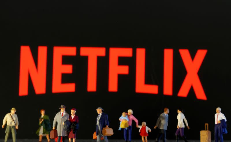 Small toy figures are seen in front of diplayed Netflix logo