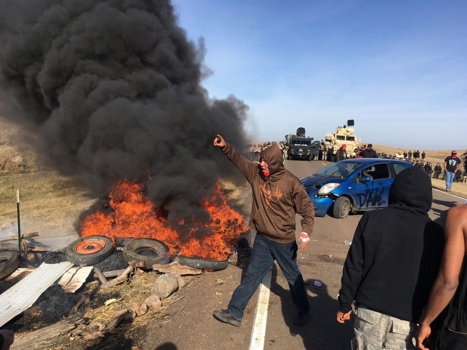 <p>Demonstrators stand next to burning tires as armed soldiers and law enforcement officers assemble on Thursday, Oct. 27, 2016, to force Dakota Access pipeline protesters off private land where they had camped to block construction. The pipeline is to carry oil from western North Dakota through South Dakota and Iowa to an existing pipeline in Patoka, Ill. (Photo: Mike McCleary/The Bismarck Tribune via AP) </p>