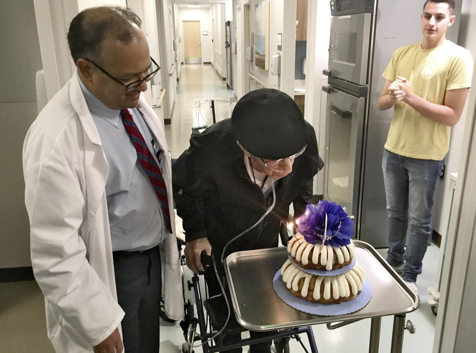 Dr. Rajneesh Nath, left, watches the Rev. John Sabbagh blow out candles on his cake for his one-year transplant anniversary as Sabbagh's grandson John, right, looks on, Friday, Sept. 7, 2018 in Gilbert, Ariz. Thirty-five years after a Mesa man cared for his son when he was shot in their native Lebanon, the son is returning that devotion. Both the Rev. John Ibraham Sabbagh and his 54-year-old son, Ebby Sabbagh, are celebrating one year of going strong since the elder Sabbagh received a crucial stem-cell transplant. (AP Photo/Terry Tang)
