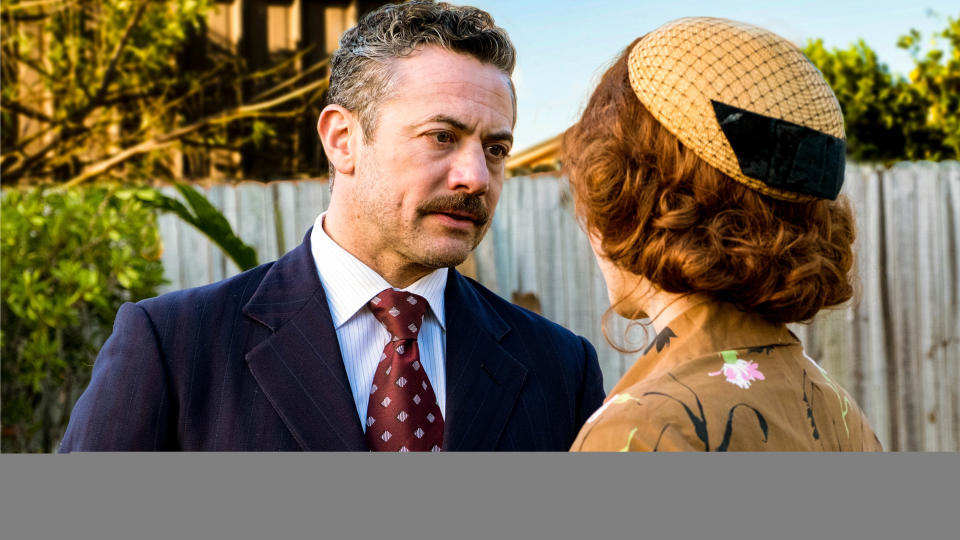 Terry (Warren Brown) in a full suit talking to Annie (Faye Marsay) in Ten Pound Poms