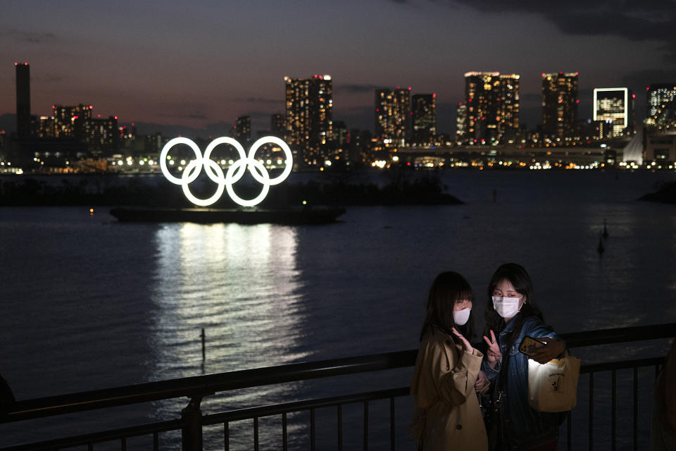 Two women take a selfie with the Olympic rings in the background in the Odaiba section of Tokyo, Thursday, March 12, 2020. Tokyo Governor Yuriko Koike spoke Thursday after the World Health Organization labeled the spreading virus a "pandemic," a decision almost certain to affect the Tokyo Olympics. For most people, the new coronavirus causes only mild or moderate symptoms. For some it can cause more severe illness. (AP Photo/Jae C. Hong)