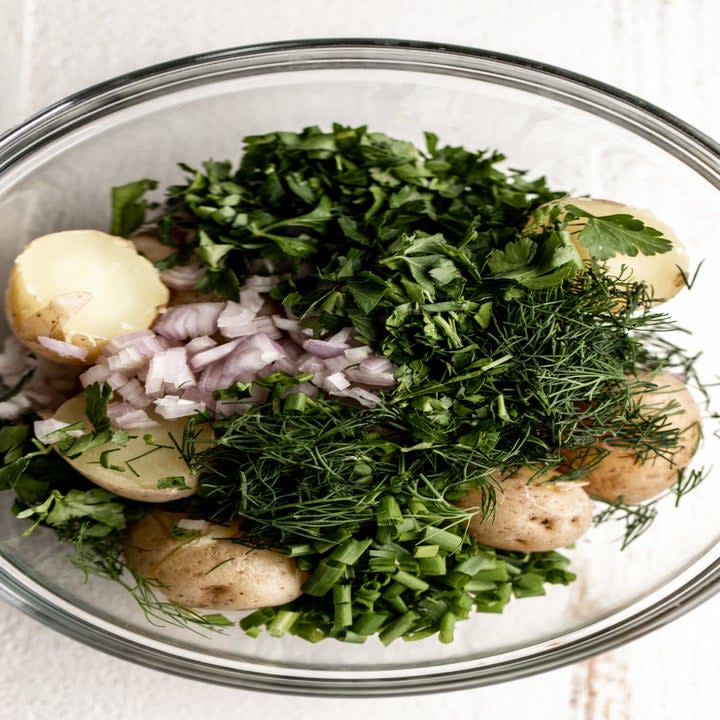 Potatoes and lots of herbs in a mixing bowl.