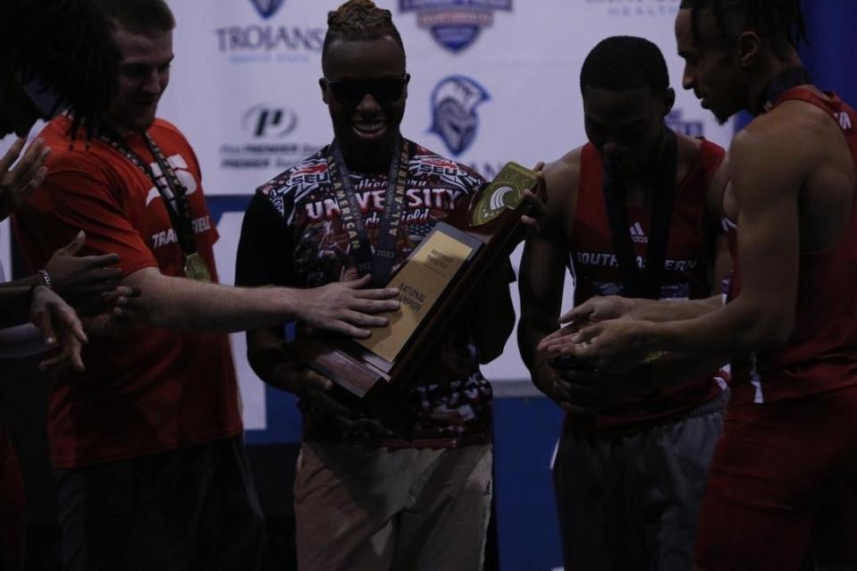 Southeastern University's Joseph Taylor, middle, holds a championship plaque. SEU won the men's track and field team title for the first time in school history in early March.