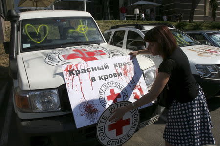 A demonstrator adjusts a placard reading "Red Cross is in blood" on a vehicle of the Red Cross during a protest to demand what protesters say is true information from the Organisation for Security and Co-operation in Europe (OSCE) about the shelling in Donetsk, Ukraine, July 23, 2015. REUTERS/Igor Tkachenko