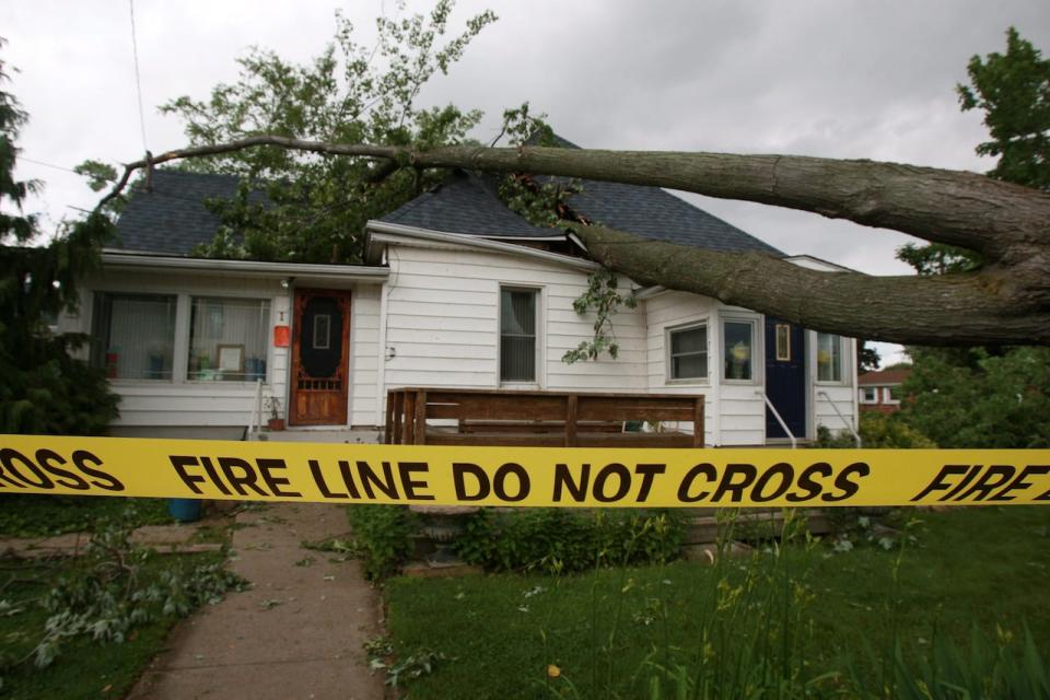 Emergency tape surrounds a damaged home with a large tree on the roof, caused by a tornado in Leamington, Ont., Sunday, June 6, 2010.  