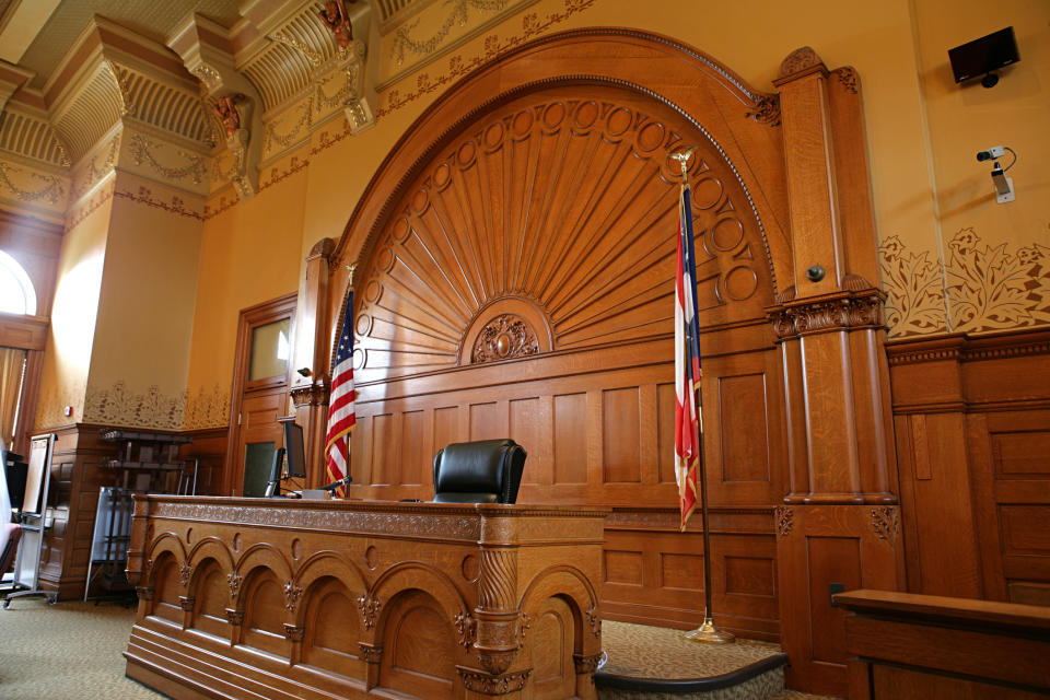 Empty judge's bench in a traditional courtroom with ornate woodwork and the United States flag to the side