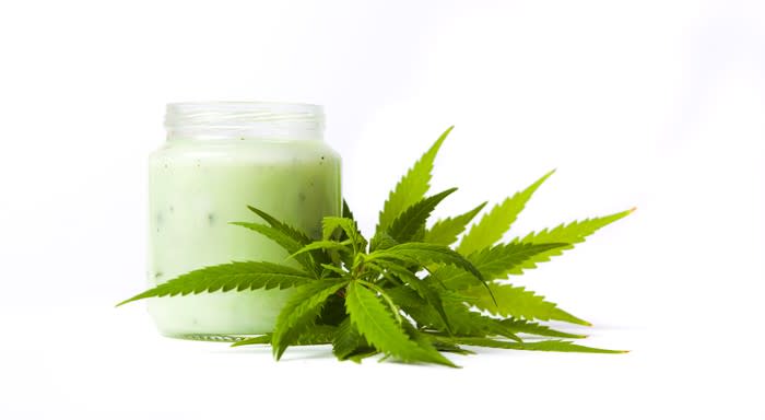 Cannabis leaves next to a full jar of topical cream.