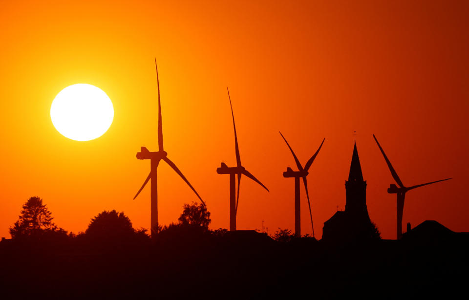 Kraftgenererende vindmølleturbiner og kirken i landsbyen er avbildet under solnedgang ved en vindpark i Bethencourt, Frankrike 11. august 2022. REUTERS/Pascal Rossignol