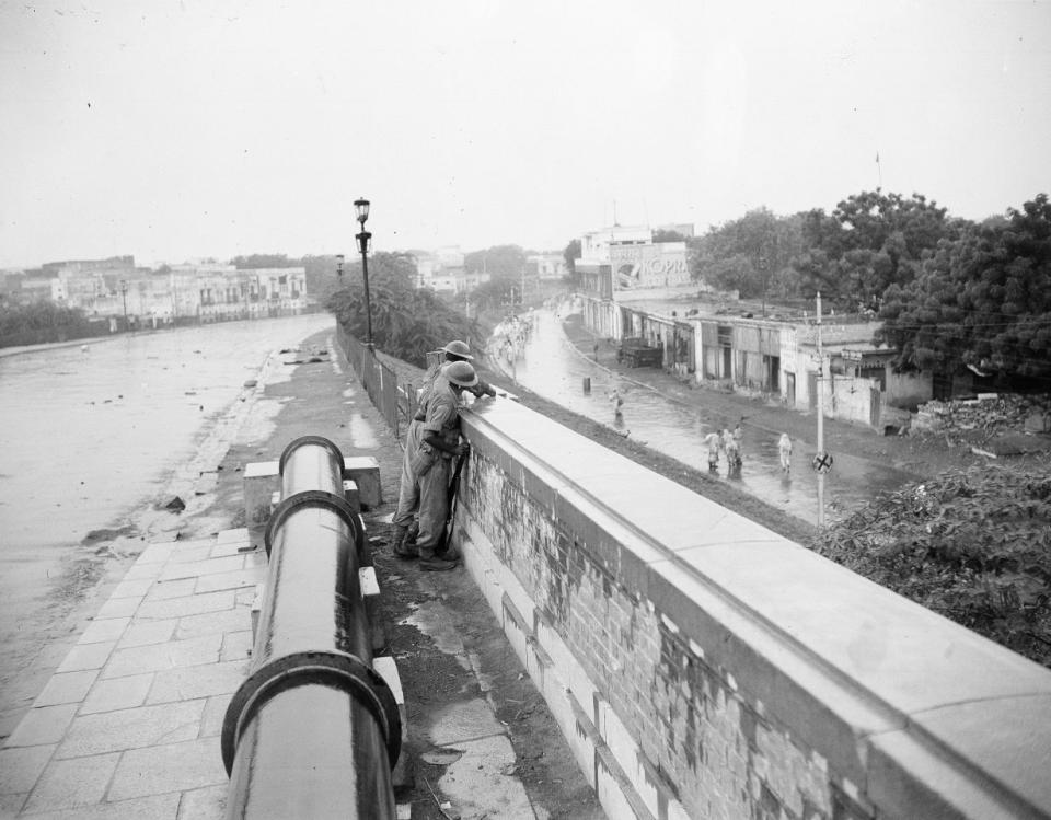 India Unrest 1947: Armed soldiers guard Muslim refugees trudging through the rain along Chelmsford Road, New Delhi, Sept. 9, 1947. On left behind soldiers are bodies of three persons killed. (AP Photo)