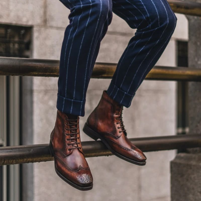 a man with a suit wearing brown wingtip boots in a back alley