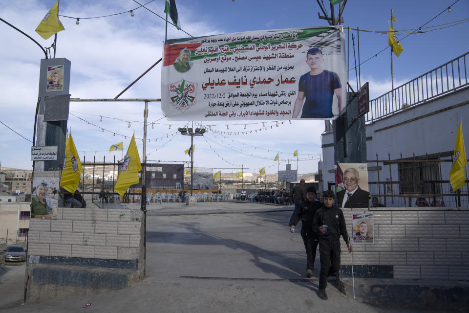 Palestinian youths walk under a poster with name and picture of Ammar Adili, 22, who was shot and killed by an Israeli border police officer on Friday, at his home village of Osreen, south of West Bank city of Nablus, Saturday, Dec. 3, 2022. Palestinians pushed back Saturday against Israeli police claims that Ammar Adili had attacked Israelis, including a border policeman, in the area and that he was shot in self-defense. They said the officer killed Adili without cause, and that Palestinian medics were kept from trying to save him as he lay gravely wounded on the side of a busy throughfare in the occupied West Bank town of Hawara. (AP Photo/Nasser Nasser)