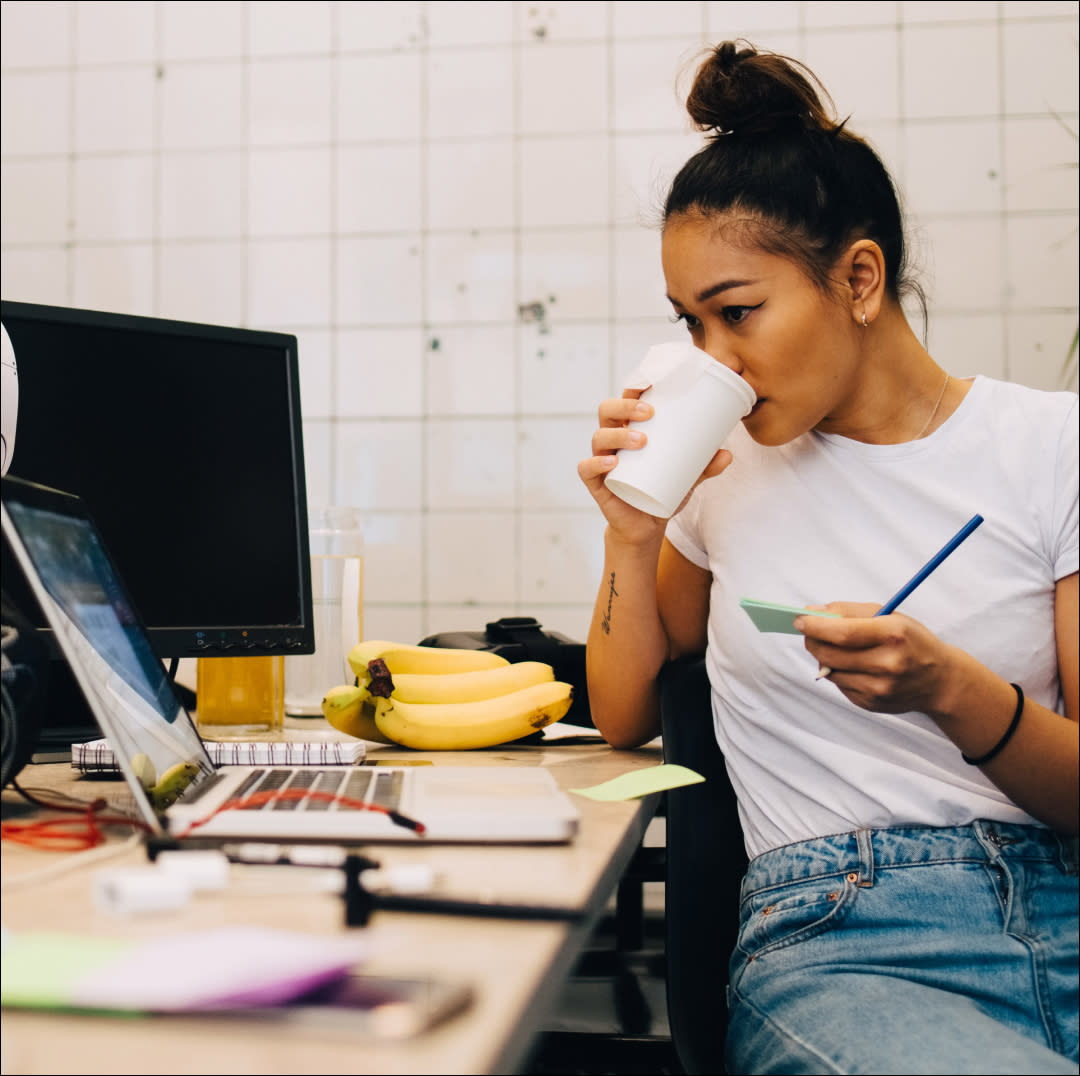  Woman drinking a cup of coffee and working at a desk with a computer 