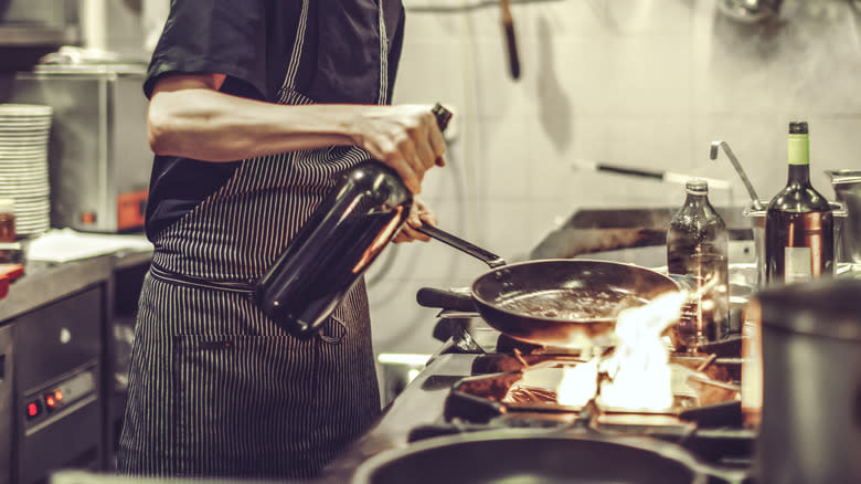 cook pouring wine into pan