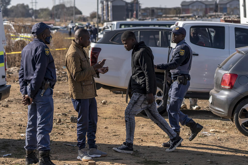 A man is led away from the scene of an overnight bar shooting in Soweto, South Africa, Sunday July 10, 2022. A mass shooting at a tavern in Johannesburg's Soweto township has killed 15 people and left others in critical condition, according to police. Police say they are investigating reports that a group of men arrived in a minibus taxi and opened fire on some of the patrons at the bar shortly after midnight Sunday. (AP Photo/Shiraaz Mohamed)