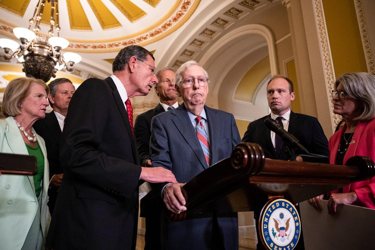Mitch McConnell grips a podium and seems unable to move as other people look on with concern.