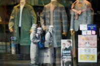 Employees from a disinfection service company are reflected in a shop's window as they sanitize a shopping district in Seoul