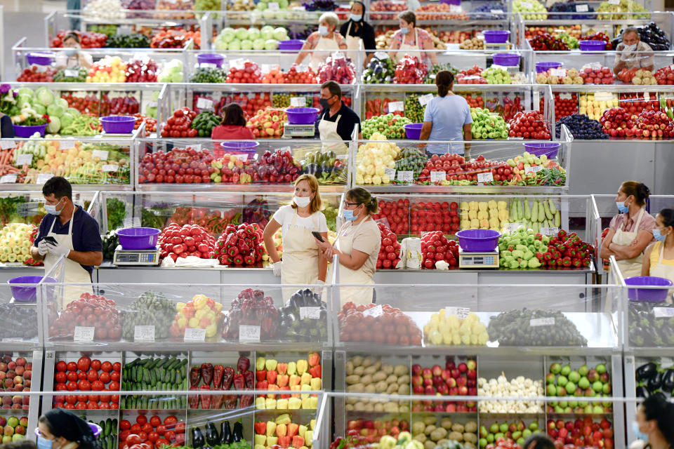 Fruit and vegetable vendors, wearing masks against the spread of the COVID-19 infections, wait for customers at a market in Bucharest, Romania, Tuesday, Aug. 11, 2020. Romania is faced with an increasing number of COVID-19 infections and related deaths over the past weeks, the highest levels since the pandemic started in the country in February, blamed mostly on people not observing the prevention regulations, like correctly wearing a face mask. (AP Photo/Andreea Alexandru)