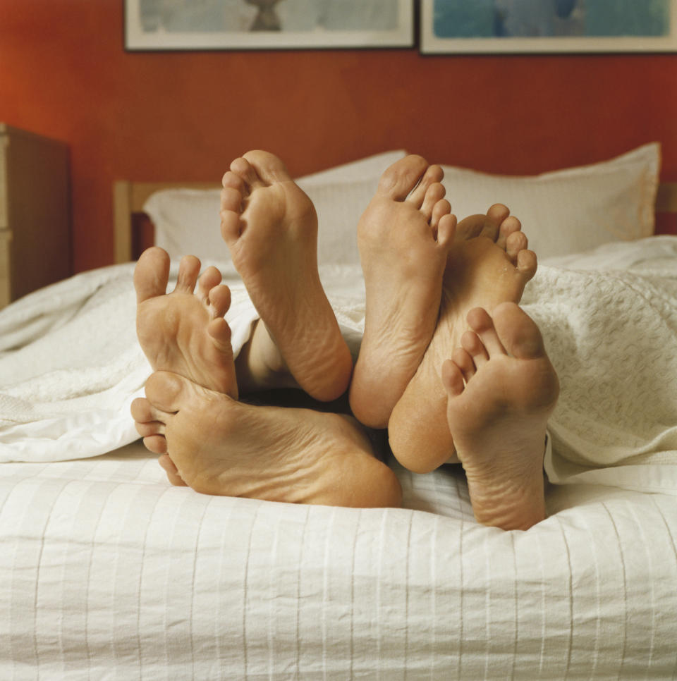 Four bare feet poking out of a blanket on a bed, implying a couple under the sheets