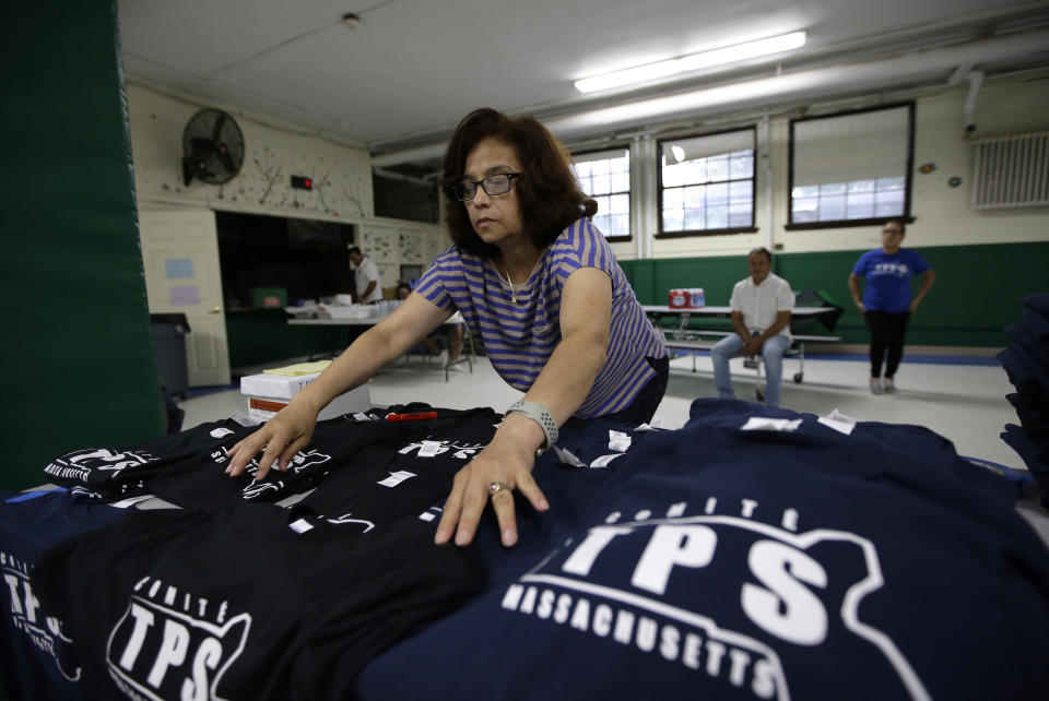 In this Sunday, June 30, 2019 photo Bertha Aleman, of Chelsea, Mass., and originally from El Salvador, arranges tee shirts featuring the Temporary Protected Status logo at a TPS meeting in Somerville, Mass. TPS is a program that offers temporary legal status to some immigrants in the U.S. who can't return to their country because of war or natural disasters. The sale of the tee shirts is meant to benefit the TPS program. (AP Photo/Steven Senne)