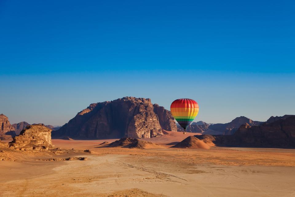 A rainbow-coloured hot air balloon takes off from the desert.